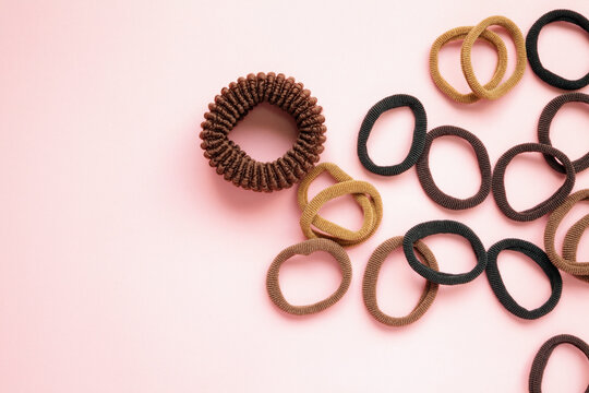 Many Elastic Hair Ties Of Natural Colors On A Pink Background With Copy Space. Black, Brown, Beige, Black, Thin And Thick Hair Holders