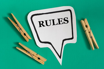 RULES - word on white sticky note with wooden clothespins on green background