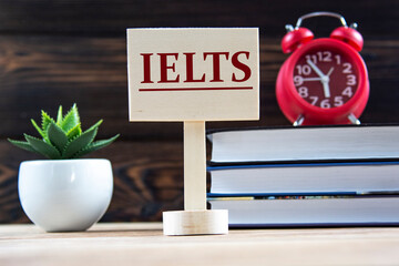 IELTS - a word on a wooden board against the background of books, an alarm clock, a cactus