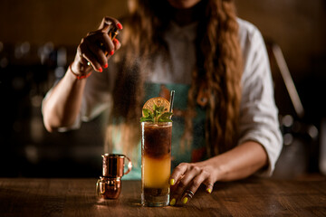 glass with coffee cocktail stands on the table and female bartender sprinkles on it