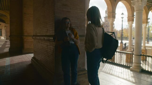 Two female students stand in university hall and discuss school project or homework assignment. Best friends chat and talk about studies in college settings. University lifestyle