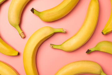 Top view photo of unpeeled yellow bananas on isolated pastel pink background