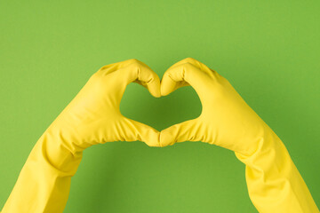 Above photo of hands in yellow gloves doing the gesture as heart isolated on the green background