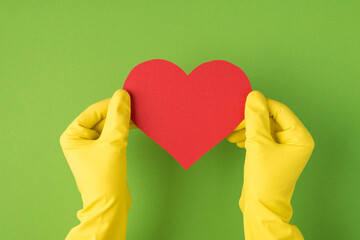Above photo of hands in yellow gloves holding the pink card as heart isolated on the green background