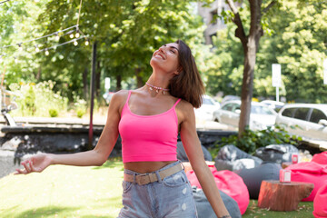 Beautiful woman in bright pink top and casual jean shorts wears beaded necklace in summer outdoor cafe positive smile enjoying summer cheerful