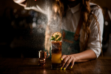 Close-up of glass with coffee cocktail and female bartender carefully sprinkles on it
