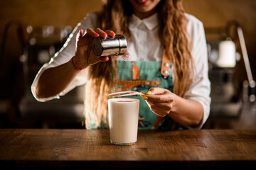 woman bartender holds stencil over glass of milk drink and sprinkles cocoa powder on it