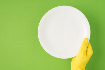 Above photo of hands in yellow gloves holding a plate isolated on the green background