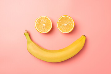 Top view photo of smiling face made from two lemon halves and banana on isolated pastel pink background