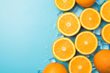 Top view photo of ice cubes drops halves and whole oranges on the right on isolated pastel blue...