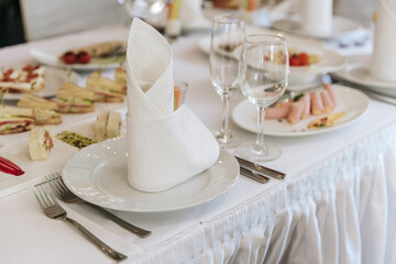 Table setting for a banquet or celebration. Empty wine glasses for spirits, champagne and juice. Set the table. Cloth napkins on a platter. Banqueting hall. Cold appetizers and salads