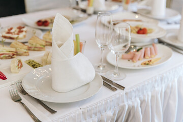 Table setting for a banquet or celebration. Empty wine glasses for spirits, champagne and juice. Set the table. Cloth napkins on a platter. Banqueting hall. Cold appetizers and salads