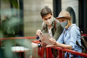 Happy tourist couple wearing protective face mask on their vacation and looking at the map.