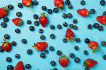 Above photo of pile of blueberries strawberries everywhere and drops of water isolated on the blue background
