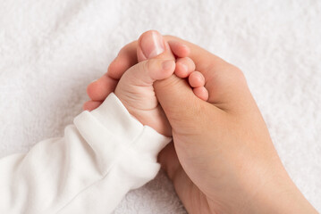 Closeup photo of newborn's tiny hand squeezing mother's thumb on isolated white textile background