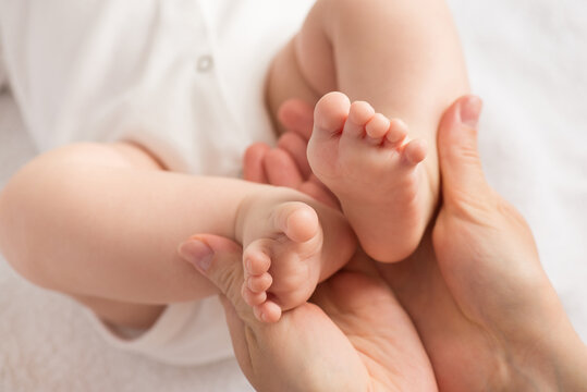Closeup photo of mother's hands holding newborn's tiny feet on isolated white textile background