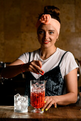 female bartender holds bar spoon in hand and stirs cold cocktail in mixing cup