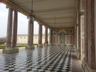 Couloir extérieur à côté du domaine de Marie-Antoinette, domaine ou demeure royal ou de reine, colonnes de marbres colorés, lampadaires historiques et carrelage brillant et géométrique
