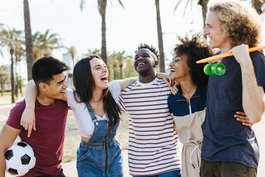 Happy friends from diverse cultures and races laughing and having fun at public park - Multi-ethnic group of young people enjoying on their summer holidays at the beach - Millennial and multicultural