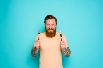 Happy man with tattoos is ready to eat with cutlery in hand