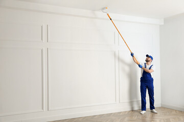 Handyman painting ceiling with white dye indoors, space for text