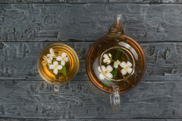A glass teapot and a bowl with lime flowers on a black wooden table.