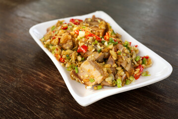 Stir Fried Crispy Pork with Fresh Chili in a white plate, put on a brown wooden dining table.