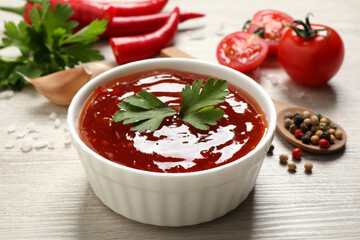 Spicy chili sauce with parsley in bowl on white wooden table