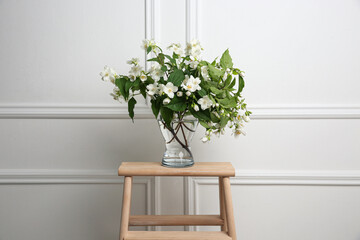Beautiful bouquet with fresh jasmine flowers in vase on wooden table indoors