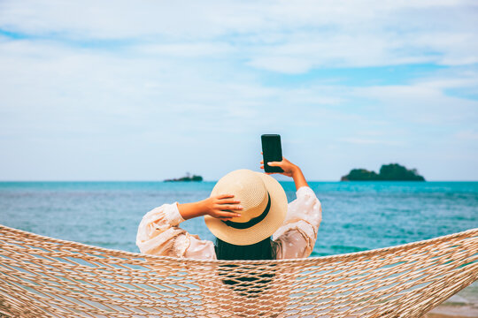 Traveler asian woman with mobile phone relax in hammock on summer beach Thailand