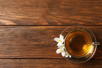 Glass cup of aromatic jasmine tea and fresh flowers on wooden table, top view. Space for text