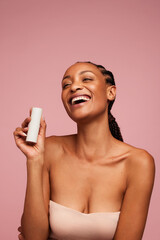 Woman holding a skincare product and smiling - obrazy, fototapety, plakaty