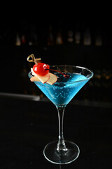 bartender special cold blue island cocktail or mocktail fruit juice with apple and cherry in tall glass goblet on black background luxury hotel pub iced beverage menu