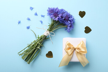 Bouquet of beautiful cornflowers and gift box on turquoise background, flat lay - obrazy, fototapety, plakaty