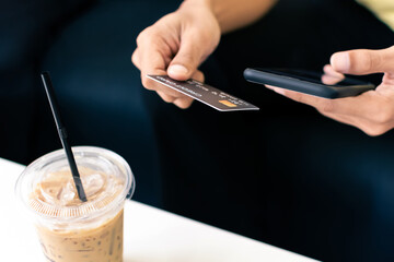 Man hand holding credit card with smartphone in coffee cafe.