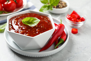 Spicy chili sauce with basil on light grey table