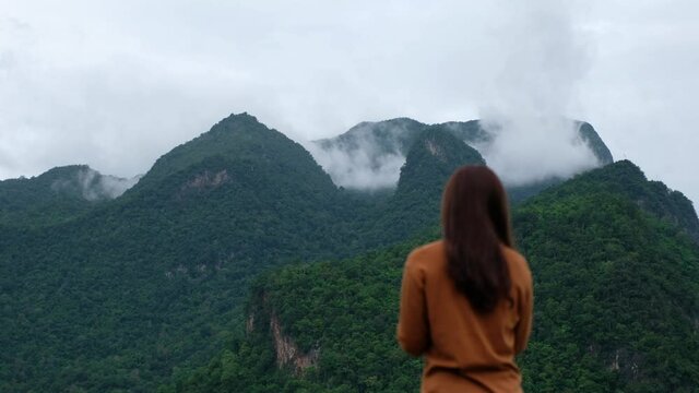 Blurred of a female traveler taking a photo of a beautiful greenery mountains on foggy day