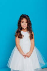 Fototapeta na wymiar Beautiful little curly girl 5 years old in a white dress on a blue background