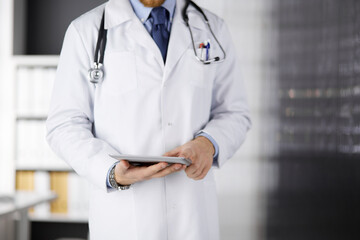 Male doctor using tablet computer in clinic, close-up. Perfect medical service in hospital