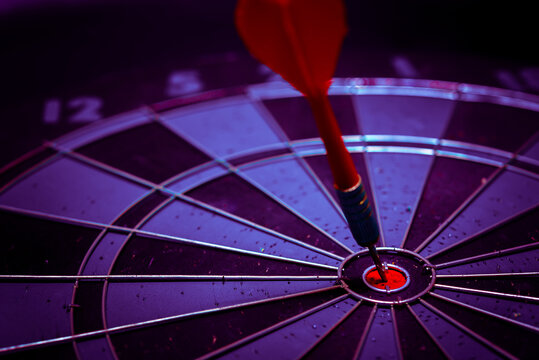 Close up shot of the dart arrow hit on bulleyes of dartboard to represent that the business reached the target of company with dark tone picture style. Target and goal as concept.	