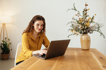 Young woman smiling happily to herself as she works on a laptop