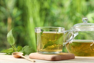 Aromatic nettle tea and green leaves on table outdoors