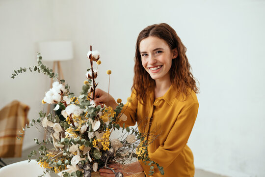 Happy joyful young woman arranging flowers at home