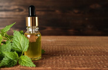 Glass bottle of nettle oil with dropper and leaves on wooden table. Space for text