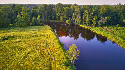 Aerial view of river in green meadows, beautiful sunset light. Evening panorama. Birch trees on riverbank.