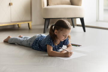Adorable little girl kid drawing in album with colorful pencils, lying on warm floor with underfloor heating at home alone, cute preschool child involved in creative activity hobby, painting
