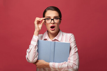 Shocked surprised woman in glasses with book with mock up copy space on red background