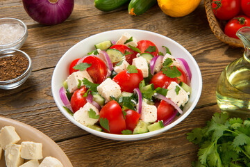 Salad with fresh tomatoes, cucumbers, red onions and feta cheese in a white salad bowl on a rustic...