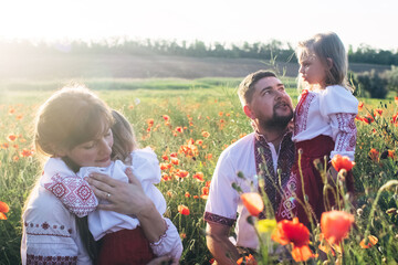 A family in a poppy field dressed in a national Slavic costume. Mom, dad and twin girls in...