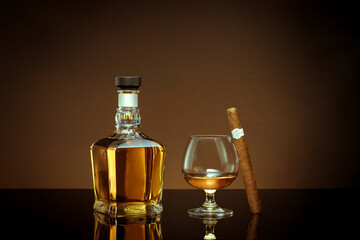 close up view of cigar, bottle of cognac and a glass aside on color back. 